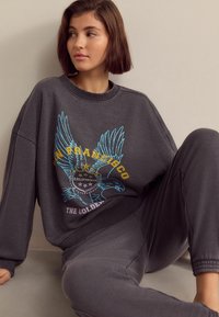 Šedá oversized mikina se barevným vyšitím s designem orla a textem "San Francisco California The Golden", spojená s ladícími kalhotami.