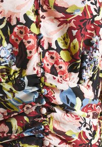Gros plan d’un tissu floral avec des parties froncées et une rangée verticale de boutons recouverts de tissu de différentes couleurs.