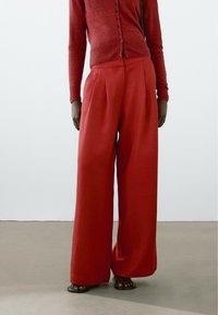 Wijd gevallen, high-waisted broeken van rode linnen met plooien, gecombineerd met een bijpassende rode aansluitende cardigan met knopen aan de voorkant.