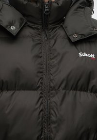 Veste matelassée noire avec fermeture éclair devant, rabats de col à boutons-pression et logo brodé blanc "Schott NYC" sur la poitrine.