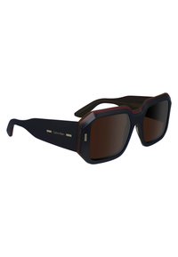 Ochelari de soare Calvin Klein cu un cadru de un albastru închis, lentile de culoare maro și accente roșii. Design pătrat cu branding subtil pe brate.