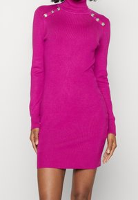 Fuchsia bodycon jurk gemaakt van zacht breiwerk, met een hoge halslijn, lange mouwen en decoratieve knopen op de schouder.