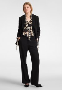 Completo nero su misura con pantaloni a gamba larga, sovrapposto a una blusa a fantasia che presenta un design crema e nero, rifinita con accenti in raso.