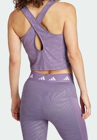 Top deportivo morado con un escote en forma de llave en la parte posterior y tirantes cruzados, combinado con leggings de cintura alta a juego que presentan un sutil patrón de cebra.