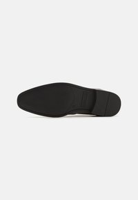 Semelle d'une chaussure habillée en cuir noir avec une surface texturée pour une meilleure adhérence et un talon carré, sur fond blanc.