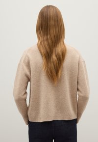 Beige gestrickter Pullover mit langen Ärmeln und einem runden Saum. Weicher Stoff, leicht übergroßer Schnitt und gerippte Akzente an den Bündchen und am Saum.
