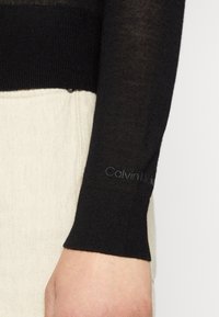 Mustassa pitkähihaisessa paidassa on ribattu alaosa ja läpinäkyvä rakenne. Hihassa on huomaamaton Calvin Klein -logo.