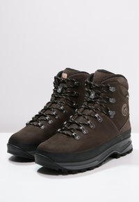 Botas de caminhada em couro castanho, com cano alto, ilhós de metal, atacadores pretos e sola de borracha texturizada para melhor aderência. Apresenta o logótipo de lado.