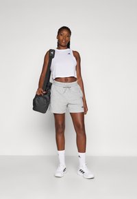 Szürke pamut rövidnadrág elasztikus derékkal és állítható zsinórral, fehér cropped top-pal és fekete sporttáskával párosítva.