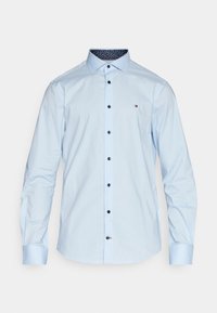 Jasnoniebieska koszula męska z długim rękawem, z ciemnymi guzikami i małym logo na piersi, z wzorzystą podszewką kołnierzyka.