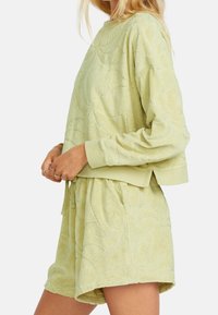 Svetle zelený loungewear set z froté, který je ozdoben texturovaným květinovým vzorem, má zkrácenou mikinu s dlouhým rukávem a šortky s elastickým pasem.