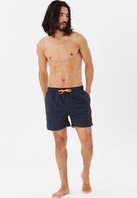 Mørkeblå badebukser i letvægtstof, med elastisk talje og orange snor. Har sidelommer og et lille logodetalje.