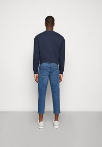 Sweatshirt azul-marinho com decote redondo, jeans de ganga azuis com corte slim e comprimento cropped, e ténis brancos. Materiais suaves e casuais.
