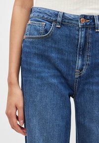 Μπλε τζιν ψηλόμεσο με φερμουάρ, σχέδιο με πέντε τσέπες, εμφανείς ραφές και ελαφρώς ξεθωριασμένη υφή.