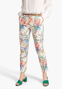 Bloemmotief broeken in het wit met roze en blauwe bloemen, slim fit, met een bruine riem en gedragen met groene open hakken.