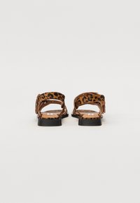 Sandales en cuir marron avec un motif léopard, dos ouvert et semelles noires plates. Les lanières ont une finition texturée pour plus de confort.