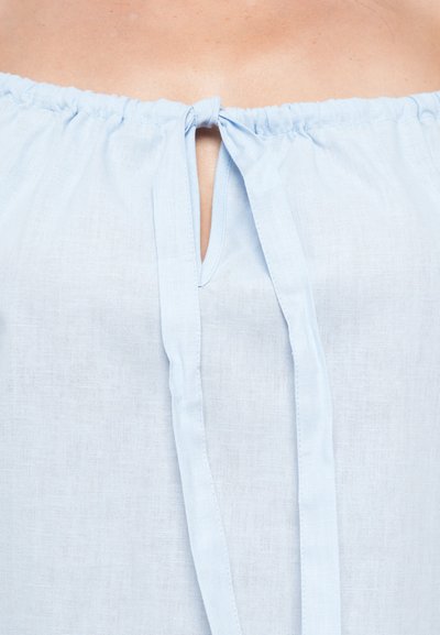 Light blue off-the-shoulder blouse made from a textured fabric featuring a keyhole opening with a bow tie detail at the neckline.