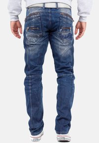 Jeans in denim blu sbiadito presentano numerosi taschini con zip, una vestibilità slim e dettagli di cucitura discreti. Abbinati a sneaker bianche.