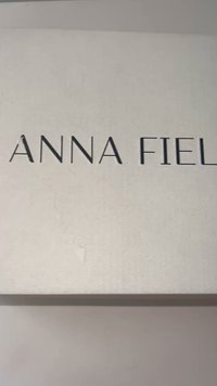 Lukket beige boks med "ANNA FIELD" trykket i store, tynne svarte bokstaver sentrert på lokket.