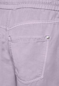 Pantalons lavande clair avec une poche arrière dotée de quincaillerie en argent. Le tissu a une texture lisse avec des détails de couture visibles.