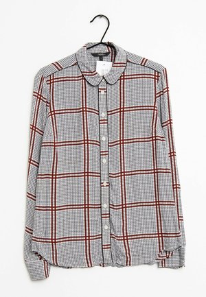 Koszula na długi rękaw zapinana na guziki, z białym, czarnym i czerwonym wzorem w kratę, wisząca na czarnym wieszaku na białym tle.