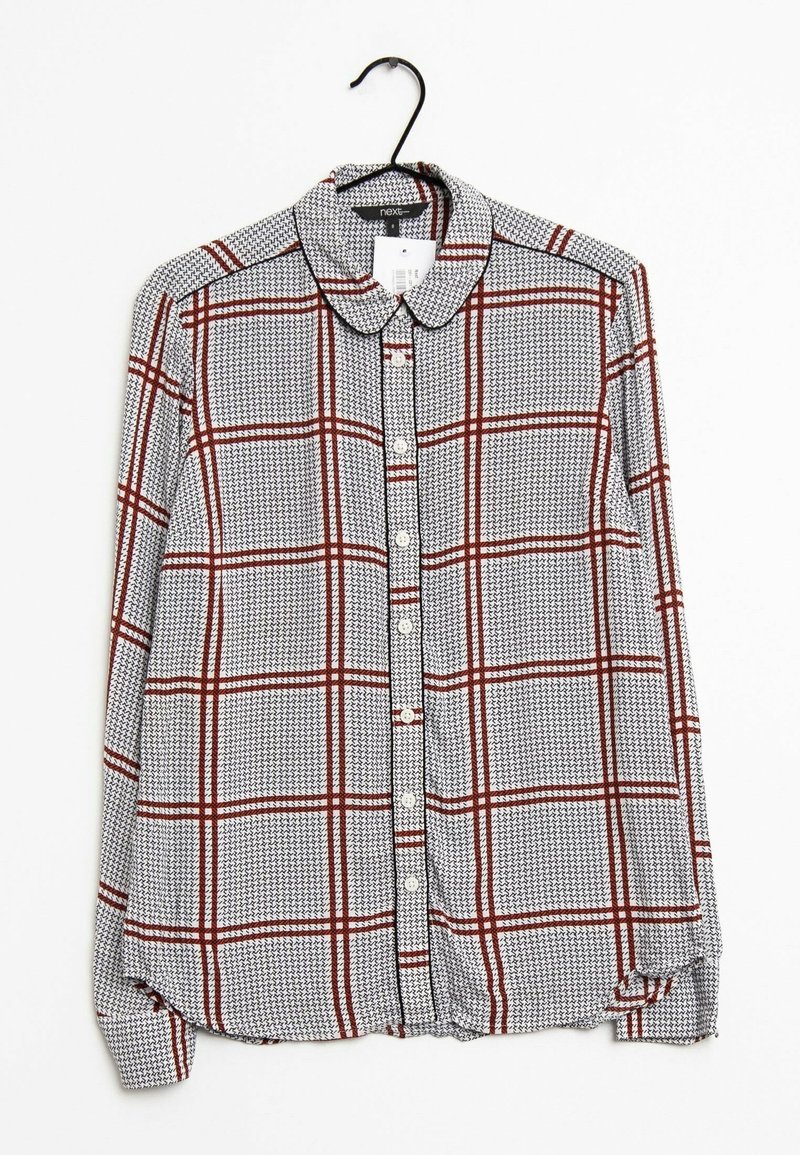 Chemise à manches longues à boutons avec un motif à carreaux blanc, noir et rouge suspendue sur un cintre noir contre un fond blanc.