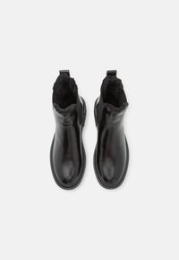 Bottes noires en cuir pour la cheville avec une douce doublure en fourrure sur le haut, présentant une finition lisse et une languette à l'arrière pour un enfilage facile.