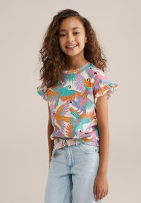 Camisa de manga corta, ligera, con estampado de pájaros coloridos en naranja, verde y púrpura. Mangas con volantes y un corte relajado. Combinada con jeans de color azul claro.