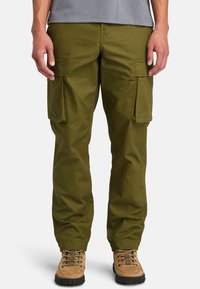 Pantaloni cargo verde oliva con due grandi tasche laterali, design a gamba dritta, tessuto resistente, indossati con stivali da escursione marroni.
