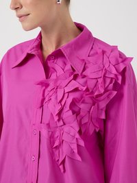 Camisa de botones de color rosa brillante con un aplique floral texturizado en el hombro izquierdo; tejido suave con cuello y mangas largas.