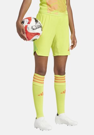 Felgekleurde gele voetbalshorts gecombineerd met bijpassende kniehoge sokken met oranje strepen. De speler houdt een meerkleurige voetbal vast.