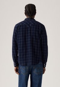 Donkerblauwe, langärmelige geruite shirt met knoopmanchetten en een gebogen schouderpas. De stof lijkt zacht met een subtiele textuur en een ruitpatroon.