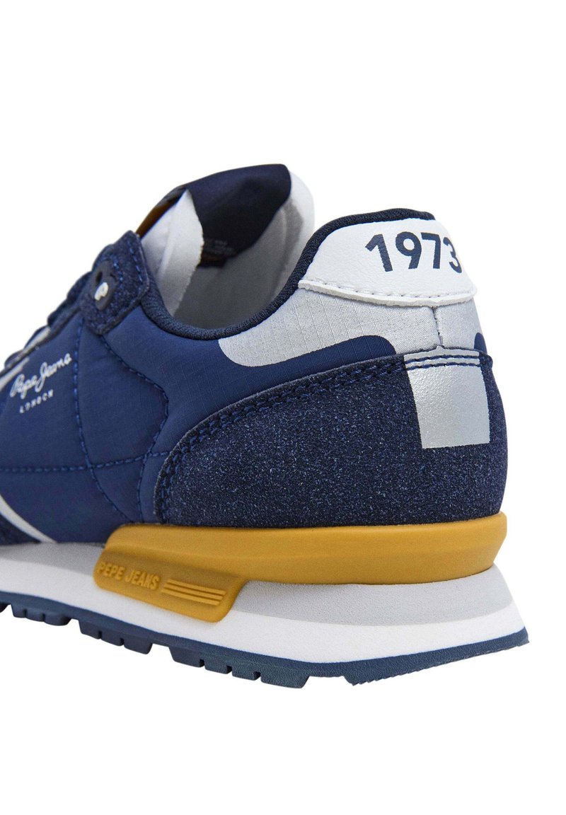 Sneakers blu navy con pannelli in suede e mesh. Presentano una suola gialla, dettagli bianchi e la scritta "1973" stampata sul tallone.