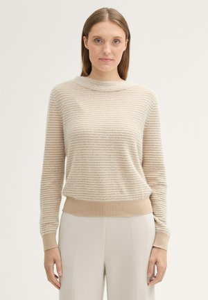 Pull en beige rayé avec un col montant, tissu à la texture douce, et des poignets et un ourlet ajustés, associé à un pantalon de couleur crème.