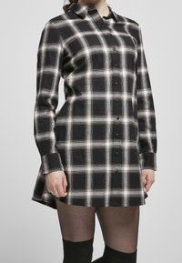 Abito camicia a quadri bianco e nero, realizzato in cotone, con chiusura frontale a bottoni, colletto e maniche lunghe, con un orlo curvo.