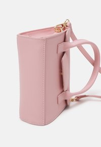 Suuri suorakulmainen vaaleanpunainen nahkakäsilaukku, jossa on yläkahvat, irrotettava olkahihna ja edessä läppä, joka on kiinnitetty kultasävyisellä soljella.