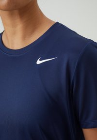 Námořnická modrá sportovní tričko vyrobené z hladkého materiálu, s bílým logem Nike na levém rameni. Krátké rukávy a design s kulatým výstřihem.