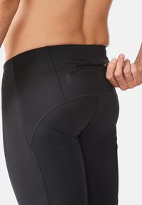 Sorte sportleggings med en glat tekstur, som har en lynlåslomme på bagsiden og synlige syningsdetaljer.