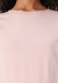 Light pink short-sleeve shirt with a ribbed crew neckline, soft texture, and a fitted design, showcasing a smooth, even surface.