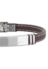 Brun läderarmband med kviltad textur, silvermetallspänne och ingraverad varumärkesnamn "BREIL", accentuerad med vit sömnad.