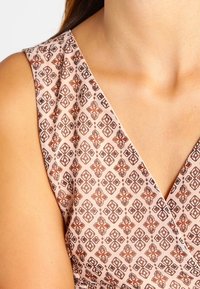 Rosa mönstrat tyg med geometriska mönster i bruna toner, med en V-ringning och texturerad yta.