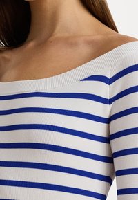 Haut à épaules dénudées, côtelé, blanc avec rayures horizontales bleues. Présente un large décolleté et un tissu texturé.