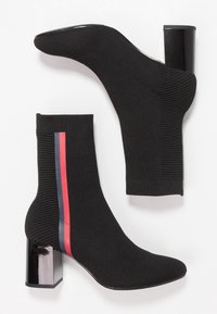 Botas de tobillo negras de punto con un ajuste similar a un calcetín, que presentan un tacón cuadrado y un acento a rayas de color rojo y azul en el costado.
