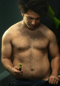 A bare-chested individual holds a yellow and black grooming device, featuring a textured grip, against a dark background with green accents.