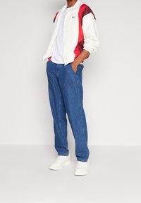 Kurtka przeciwwiatrowa w blokach kolorów białym i czerwonym, biała koszulka, niebieskie dżinsy oraz białe trampki. Swobodny krój z subtelnym logo na kurtce.