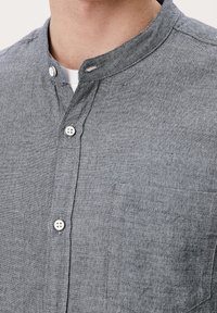 Grijs linnen overhemd met een mandariijnkraag, met witte knopen en een borstzak aan één kant. Gestructureerde stof zichtbaar, mouwen van gemiddelde lengte.