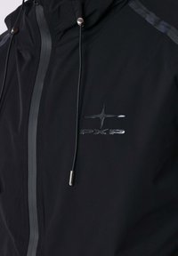 Giacca nera impermeabile con colletto alto, accessori in acciaio inox e una striscia riflettente sulla spalla. Presenta un logo sul petto.