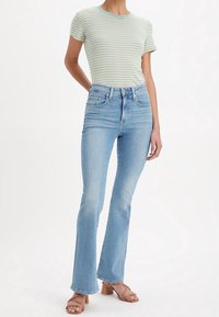 Haut à manches courtes rayé vert clair et crème, associé à un jean évasé bleu taille haute et des sandales à talons marron. Texture de tissu lisse.