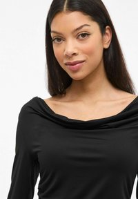 Zwart langemouwen top met een gedrapeerde halslijn, gemaakt van een gladde stof, met een getailleerde pasvorm en zachte, iets gestructureerde details.