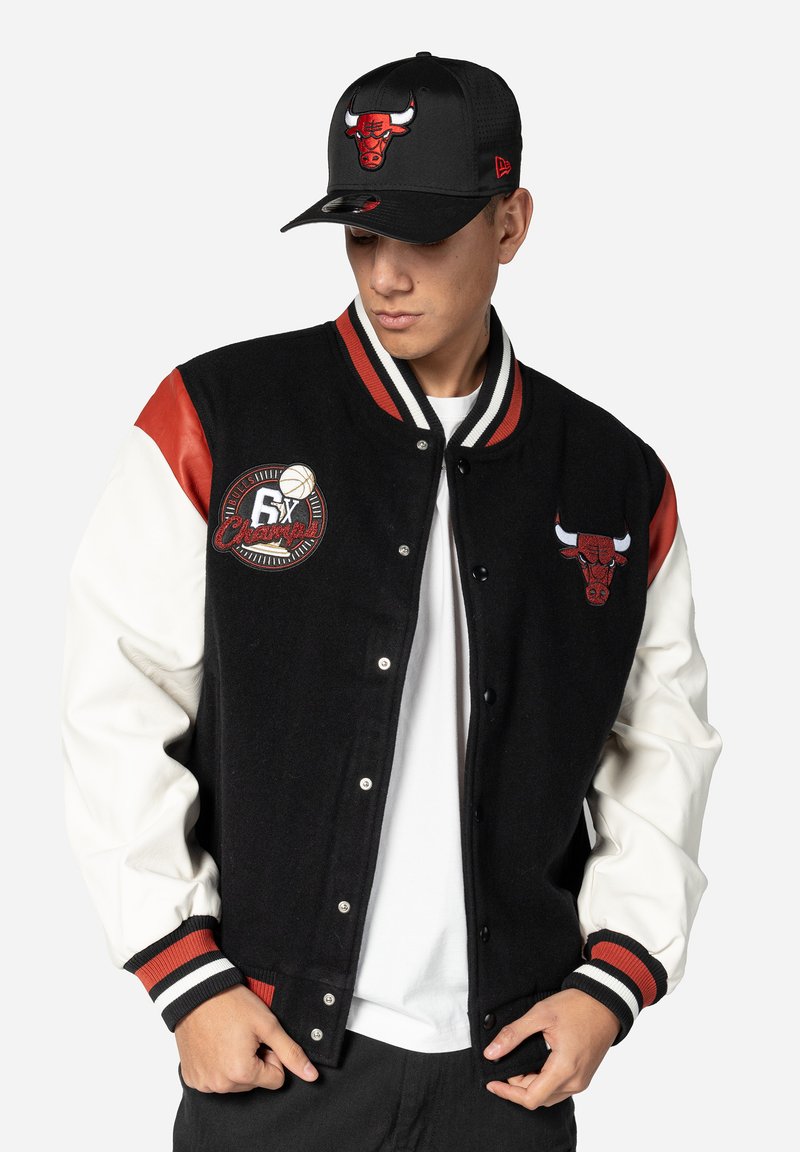 Black wool varsity jacket with red and white leather sleeves, featuring embroidered Chicago Bulls logo and championship patch. Paired with a black cap.